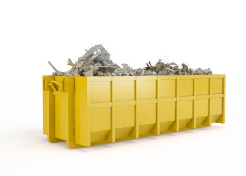 A large yellow skip bin filled with a mixture of crushed concrete, debris, and rubble, positioned on a clean, white surface. The skip features high sides composed of rectangular panels, with metal corner supports and hinge mechanisms visible on the left side. The textured and rough surface of the crushed concrete varies in shades of gray and white, contrasting with the smooth, bright yellow finish of the container. The surrounding environment appears minimalistic and professional, suggesting a controlled, outdoor or warehouse setting typical of commercial waste collections in Southwark. The image visually represents waste loading or removal activity associated with rubbish clearance services provided by Commercial Waste Southwark, highlighting the types of materials handled and the industrial appearance of waste management equipment used in urban rubbish disposal tasks.
