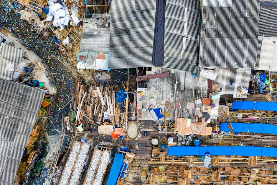 A large, cluttered pile of rusted, weathered scrap metal and debris situated outdoors, with various metal sheets, pipes, and chassis parts scattered across a rough, uneven ground of dirt and small rub